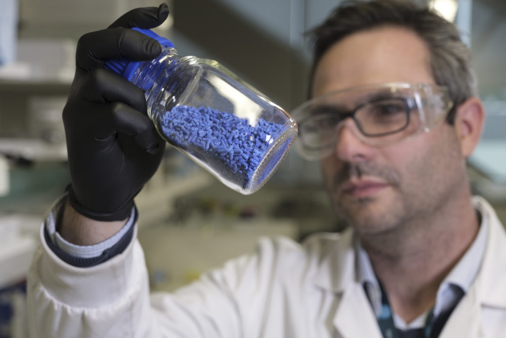 Male researcher in a lab environment examines a jar of blue pellets